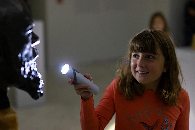 Taschenlampenführung: Ein Mädchen strahlt mit der Taschenlampe eine Bronzeskulptur an